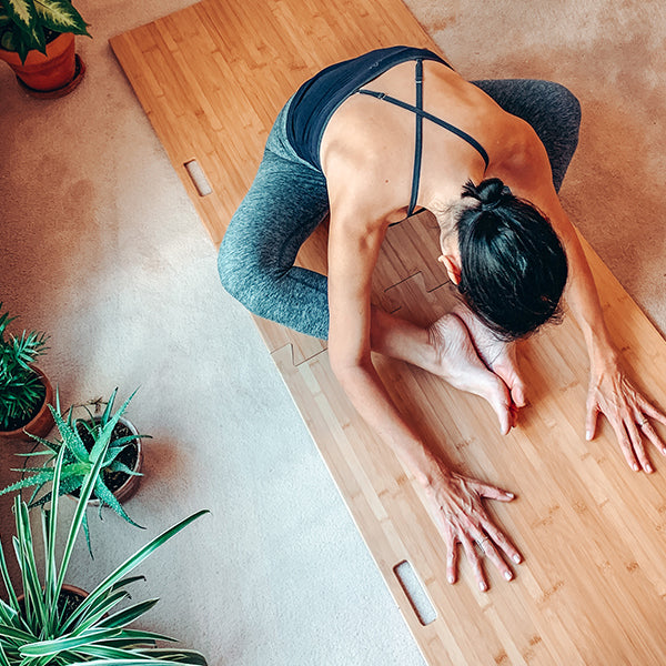 woman in resting yoga pose on Root Board on carpet